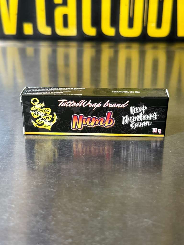 TattooWrap Numb Deep Numbing Cream box on a shiny metal surface showing 'Numb' and 'Deep Numbing Cream'.